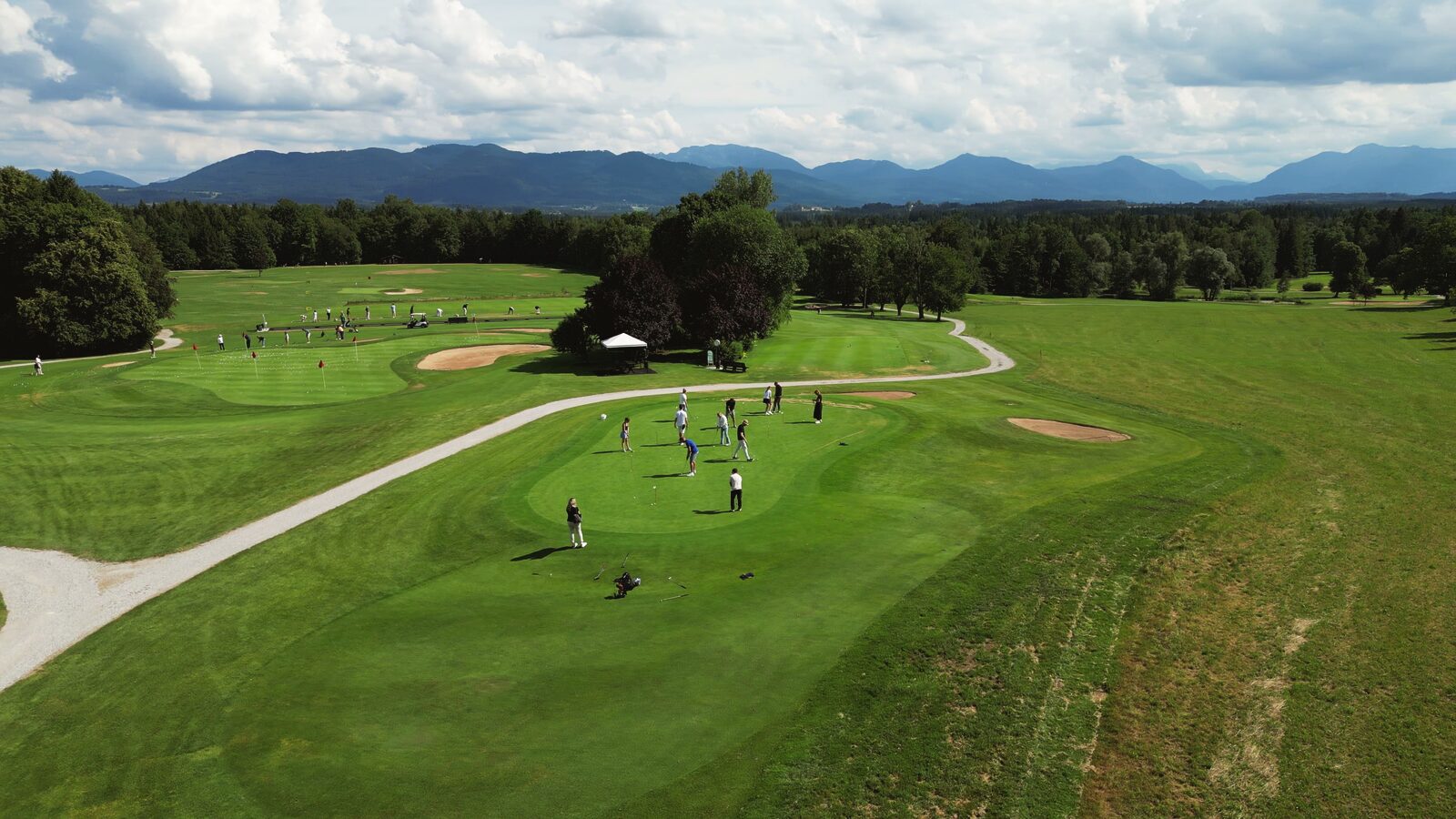 Gäste auf dem Grün beim Schnuppergolfen, dahinter die Berge