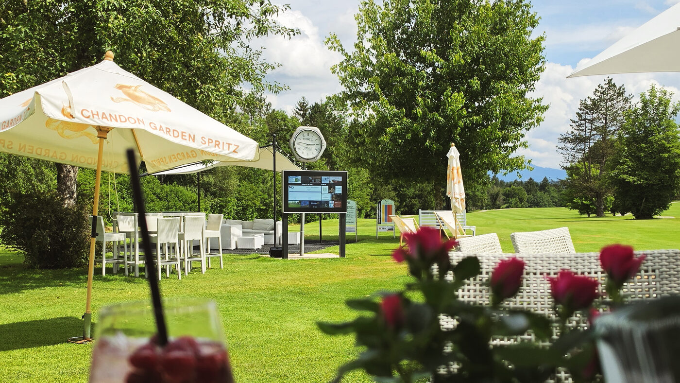 Terrasse mit Sonnenschirm und Stehtischen, daneben das digitale Display